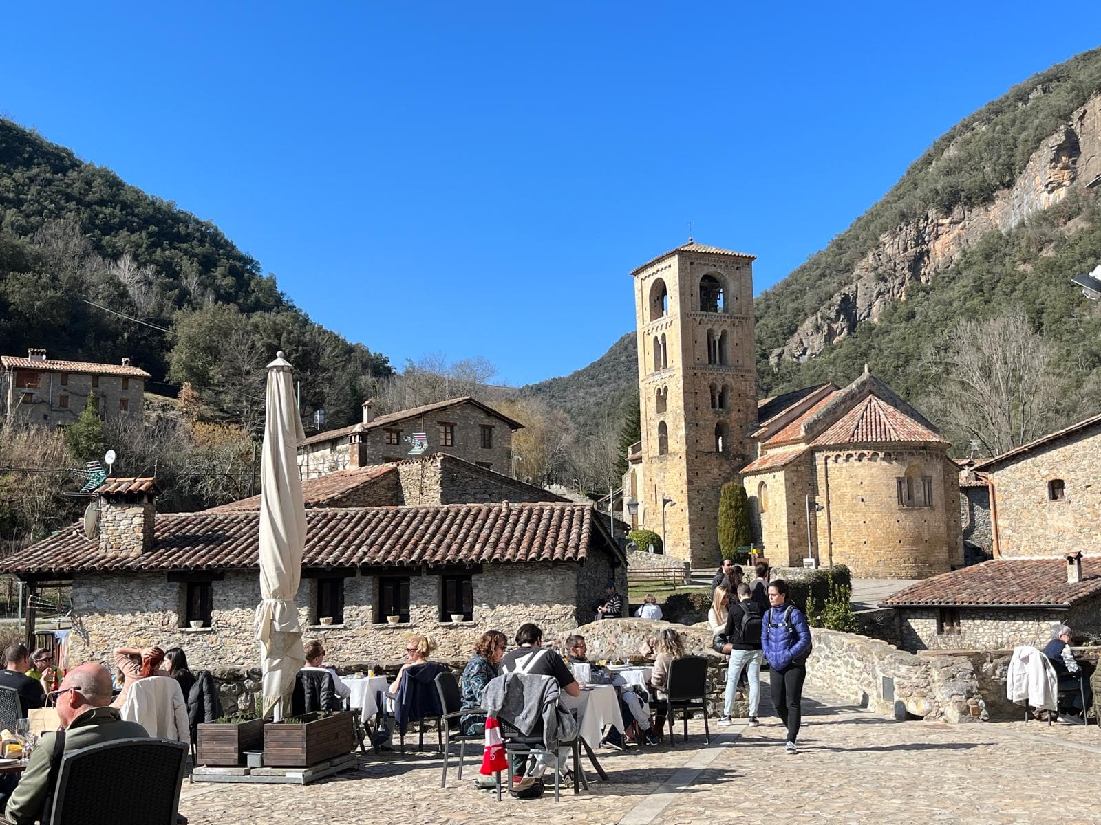 A village square with a Romanesque bell tower framed by mountains