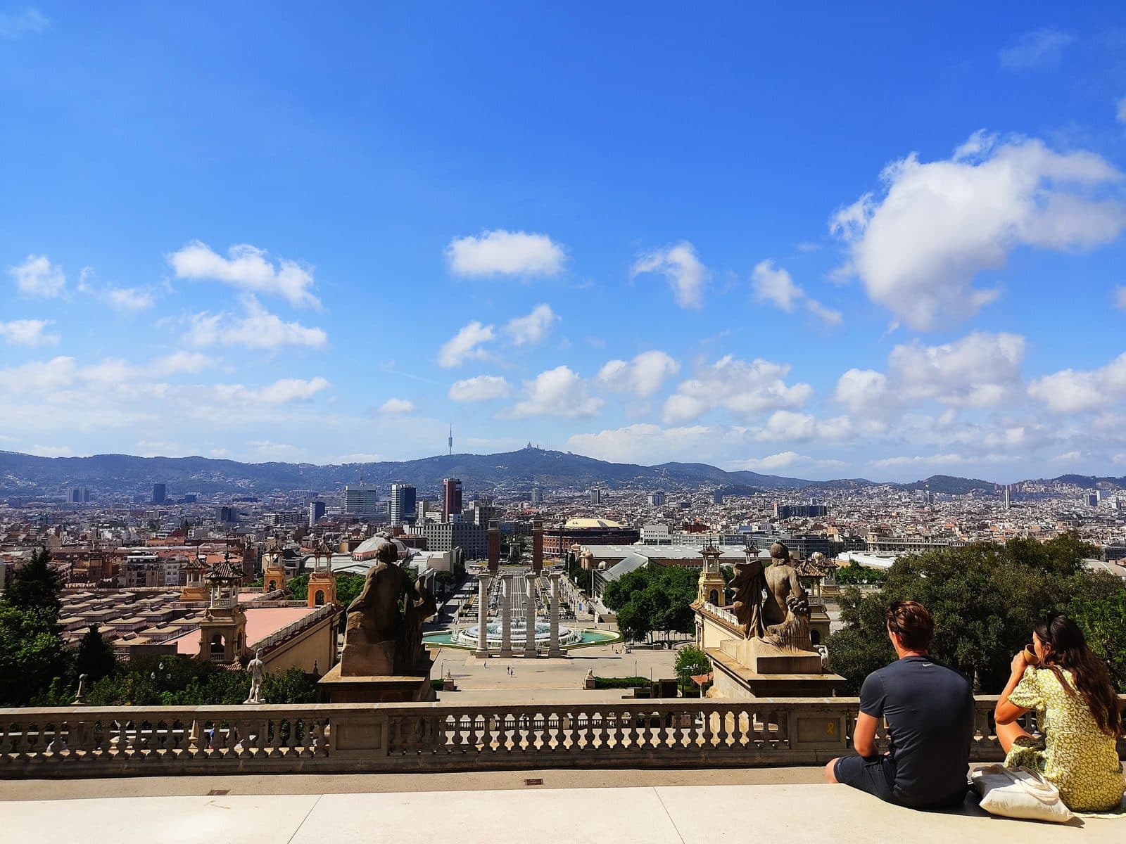 The city spread out below a Montjuïc terrace, two visitors seated taking in the view