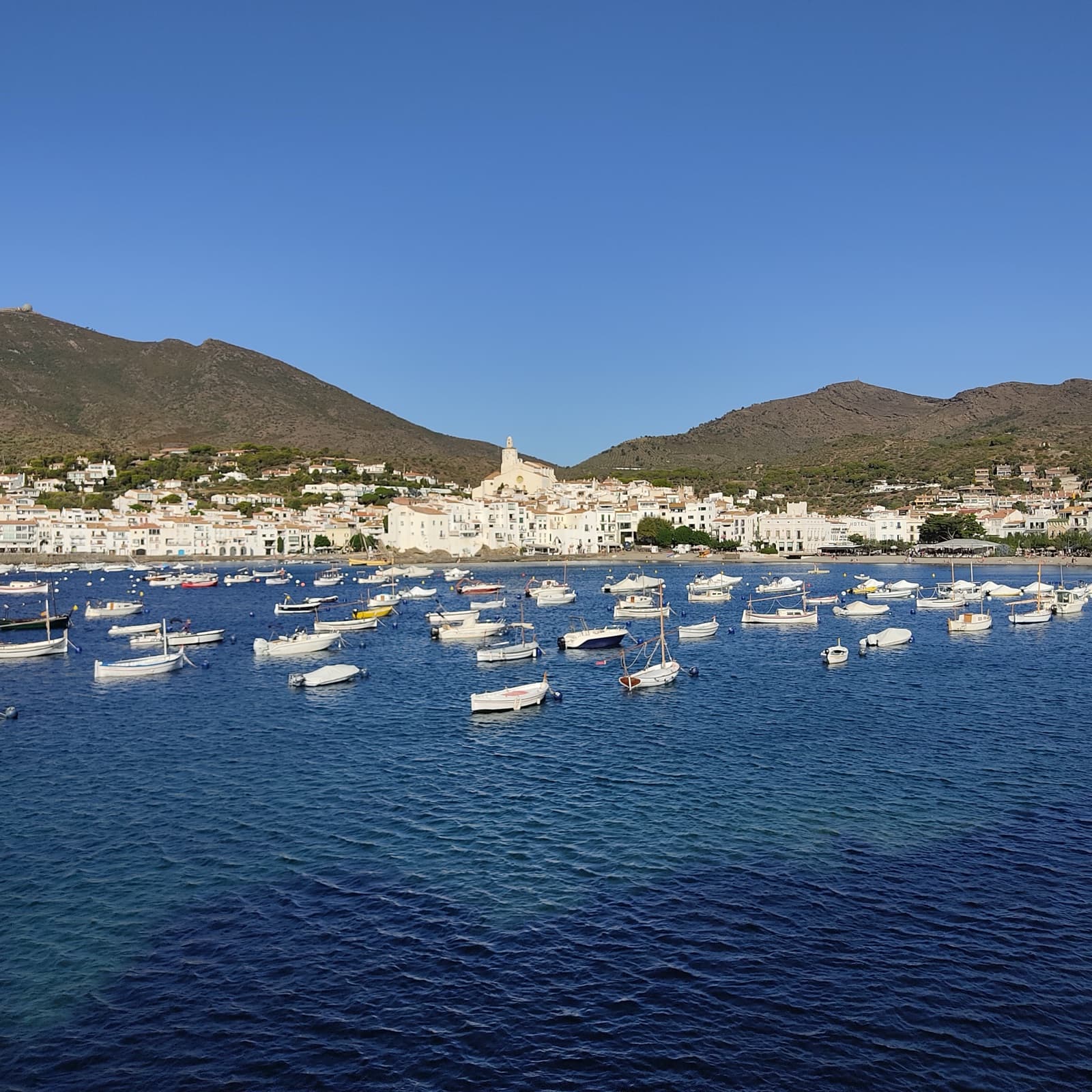 A Costa Brava bay lined with a whitewashed village and moored fishing boats below the hills