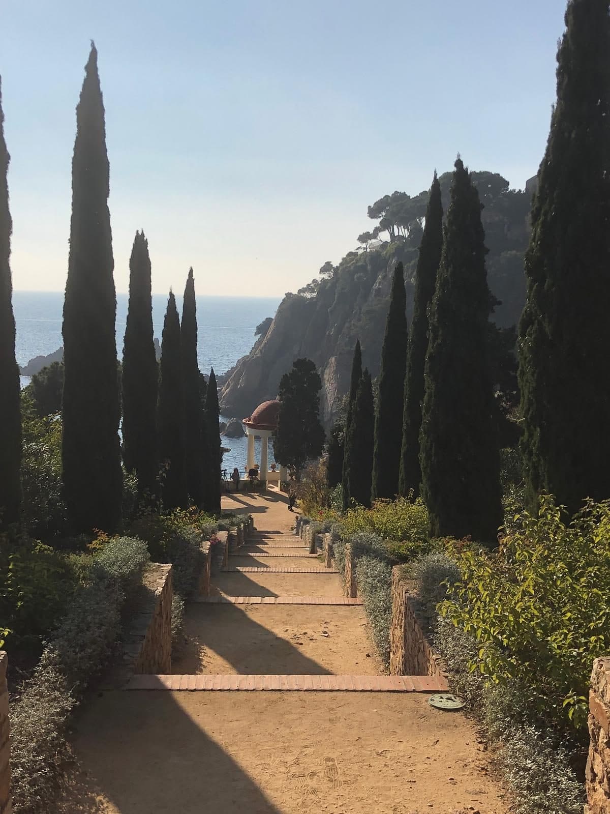 A cypress-lined garden path descending toward the sea