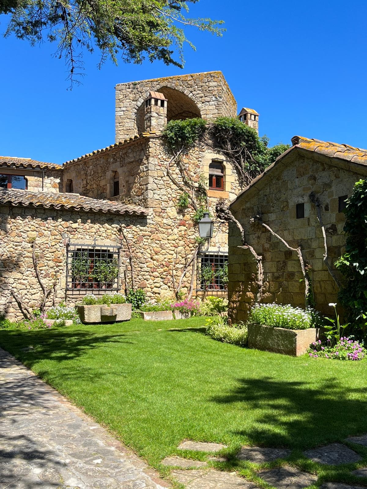 A medieval stone manor with a garden lawn in the Baix Empordà