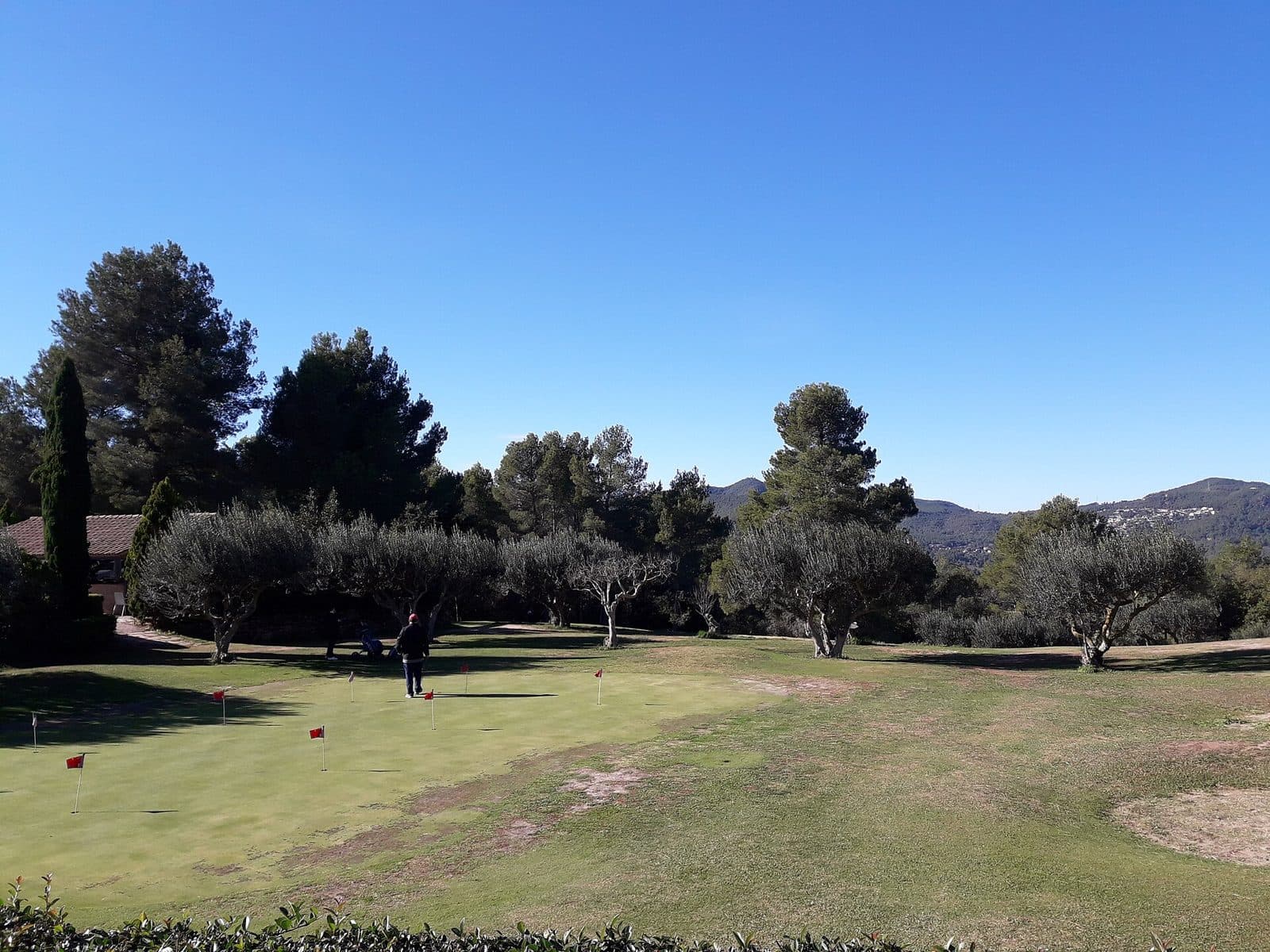 A manicured golf course fairway framed by trees under a blue Catalan sky