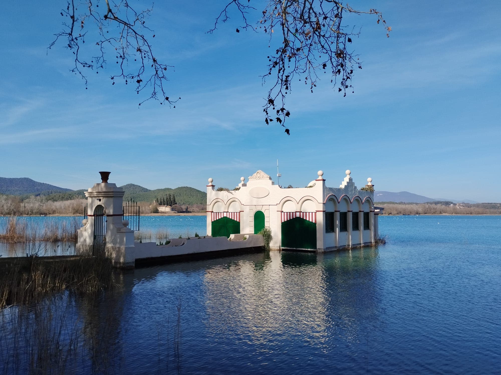 An ornate white lakeside pavilion reflected in a calm inland-Catalonia lake ringed by hills