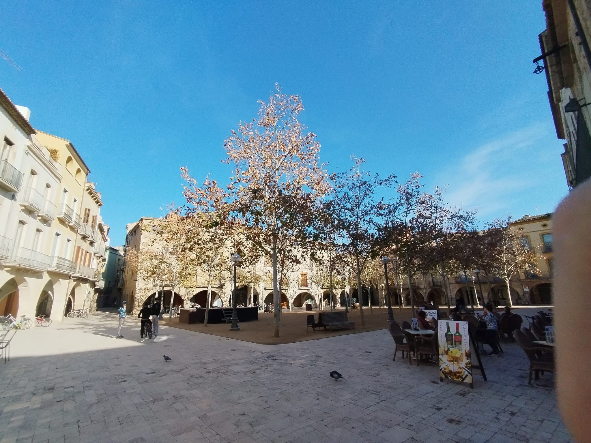A quiet arcaded village square with café tables and autumn trees