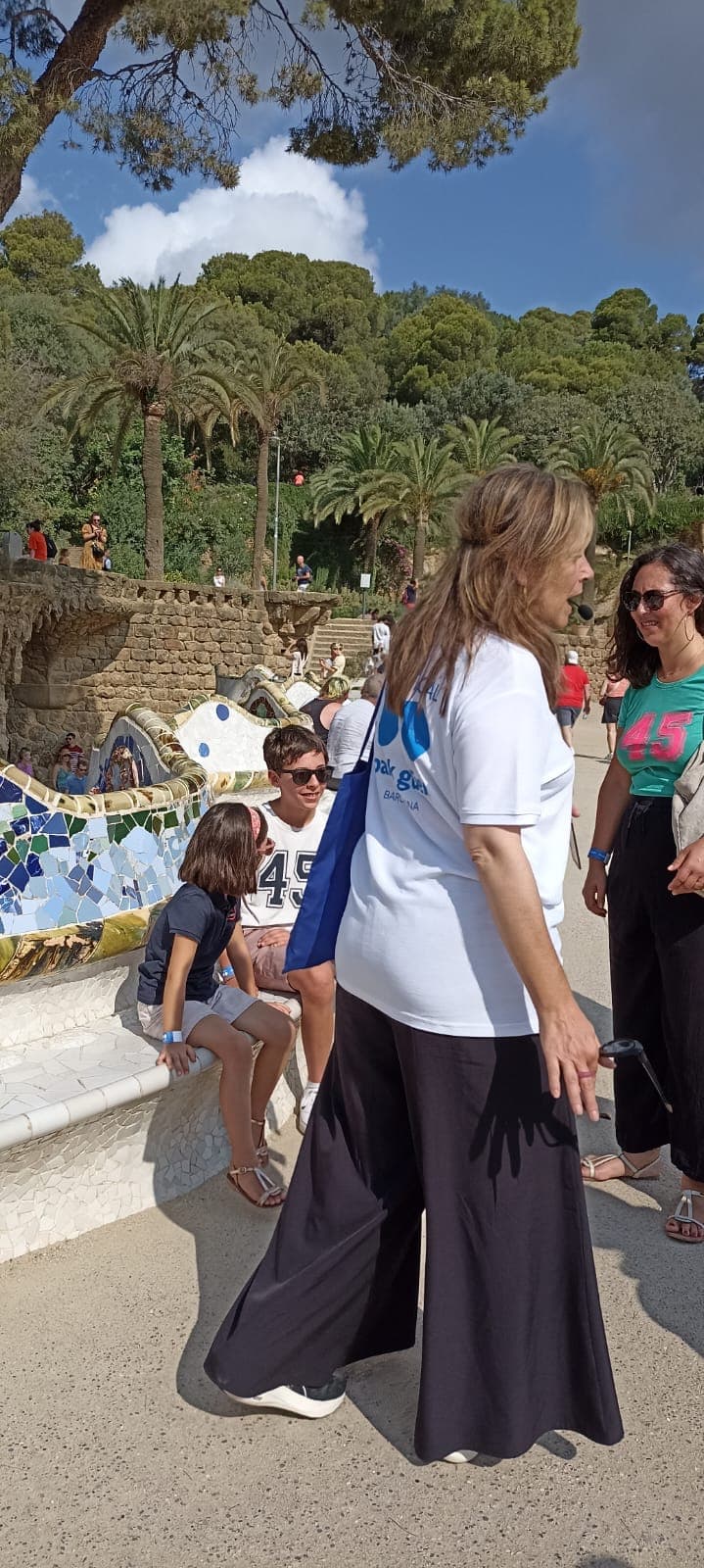 A guide explaining the serpentine trencadís bench to visitors at Park Güell