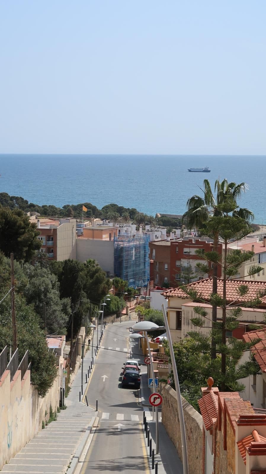 A historic Tarragona street descending toward the sea, a ship on the horizon