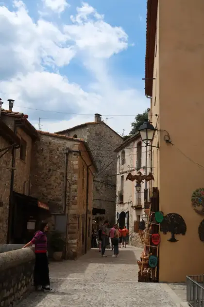 A sunlit village street lined with small shopfronts