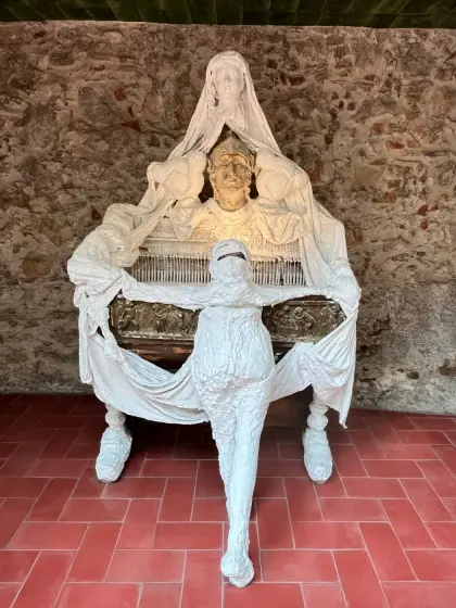 A white draped figure seated against the brick of the courtyard