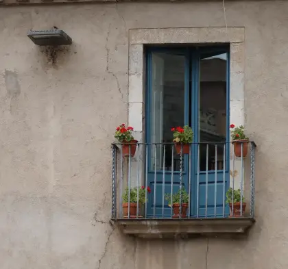 Un balcón azul con geranios en un muro desgastado