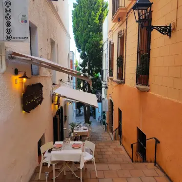 Taules parades per dinar en una terrassa estreta entre façanes de colors